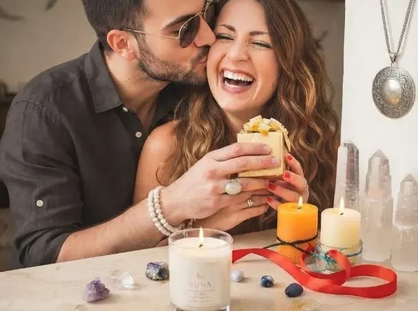 Pareja feliz celebrando en Cúcuta con un regalo, rodeados de velas artesanales Luna y cristales energéticos.